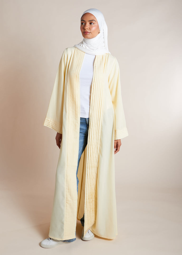 This open pleat abaya in buttercream boasts exquisite neat pleating that cascades down the placket and cuffs, offering a loose yet structured fit for all body types. Perfect as a quick cover-up for everyday outfits, or paired with one of our full slips for a more elegant ensemble.&nbsp;
